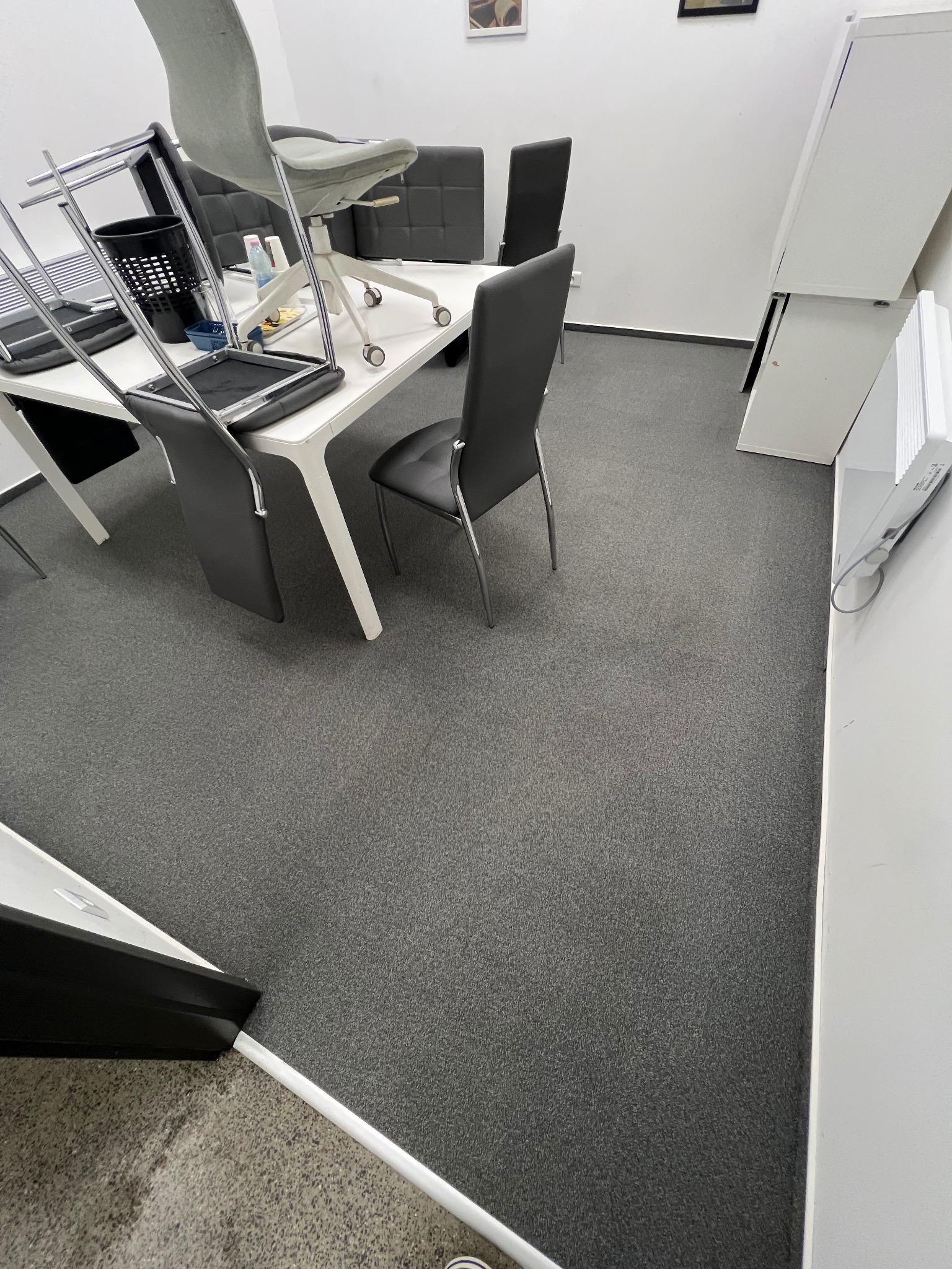 Biuro po sprzątaniu: szary dywan, białe meble, krzesła na stołach. Porządek w minimalistycznym stylu, gotowe do pracy. Widok z góry.