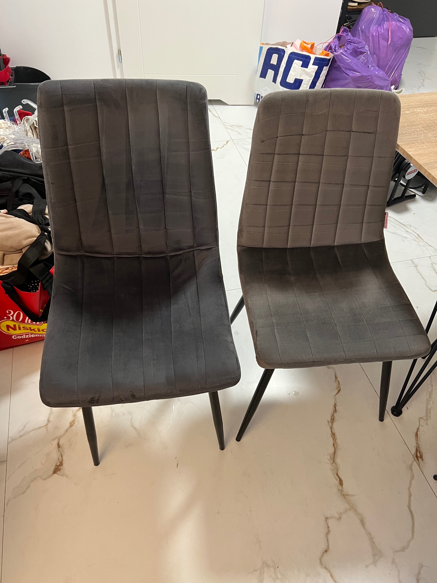 Dwa krzesła tapicerowane: szare z pionowymi przeszyciami i brązowe z kwadratowymi przeszyciami. Widoczne zabrudzenia na krześle i podłodze.