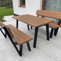 HolzWood Michał Bednarczyk - Komplet drewnianych mebli ogrodowych: stół i dwie ławki z oparciami, z czarnymi, metalowymi nogami, na jasnym tarasie, z widokiem na zielony krajobraz.