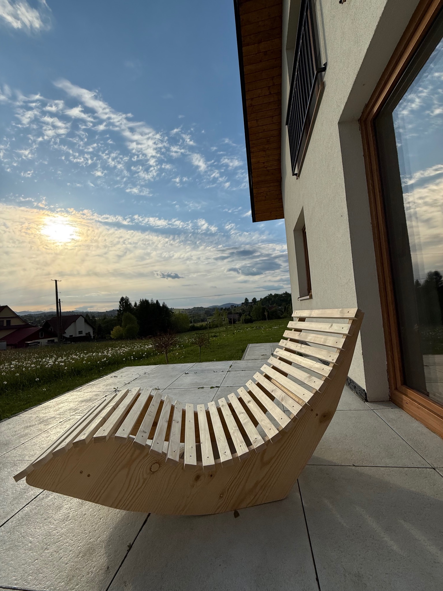 Ergonomiczne, drewniane leżanki na tarasie z widokiem na łąkę i zachodzące słońce. Nowoczesny design i naturalne materiały.