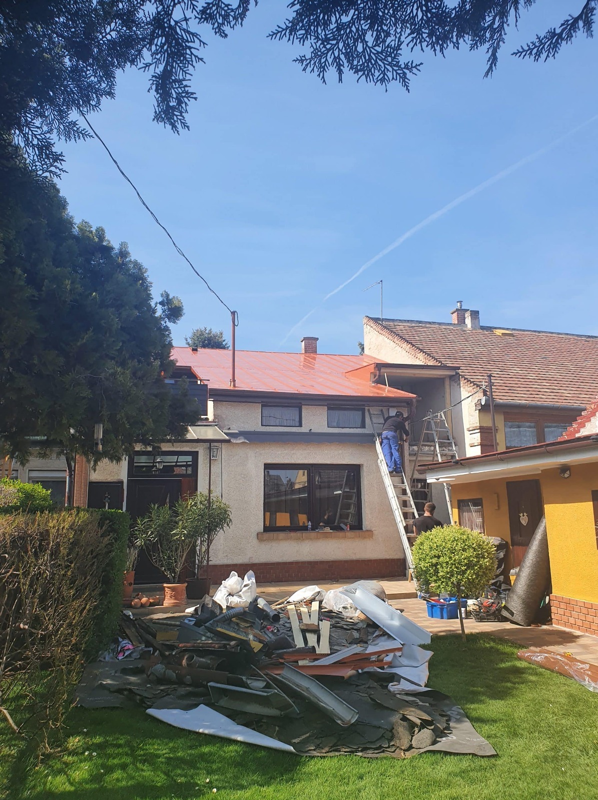 Wymiana dachu z blachy trapezowej na budynku w Katowicach. Widoczne stare elementy dachu na trawniku i pracownicy na drabinie.