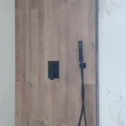 Marcin Petrykowski Wemar-Rem - Nowoczesna kabina prysznicowa z drewnopodobnymi panelami, czarną armaturą i odpływem liniowym. Minimalistyczny design, marmurowe wykończenie ściany.