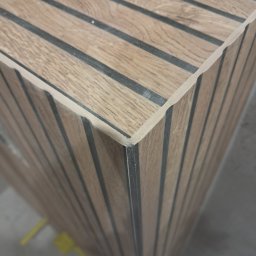 Marcin Petrykowski Wemar-Rem - Wykończony narożnik obudowy z paneli drewnopodobnych z czarnymi fugami, widoczny z bliska pod kątem, ukazujący precyzję wykonania i estetykę detalu.