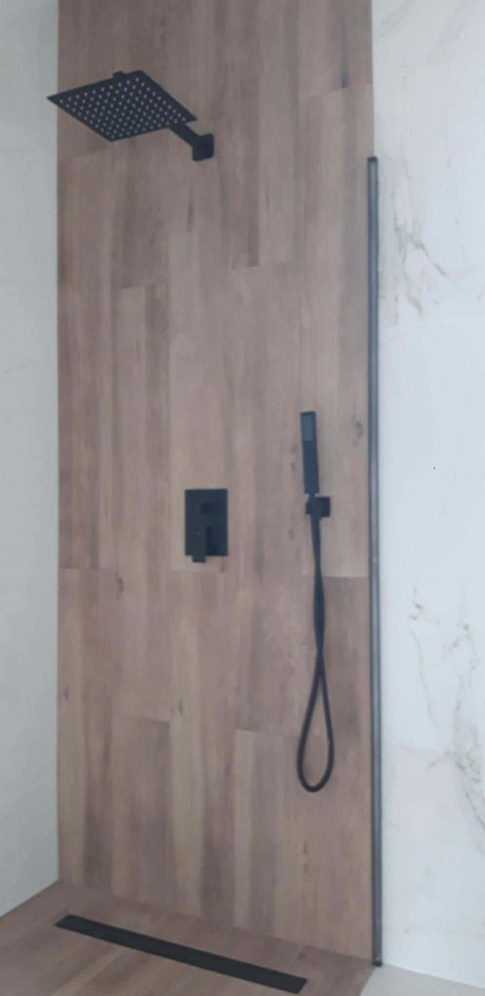 Nowoczesna kabina prysznicowa z drewnopodobnymi panelami, czarną armaturą i odpływem liniowym. Minimalistyczny design, marmurowe wykończenie ściany.