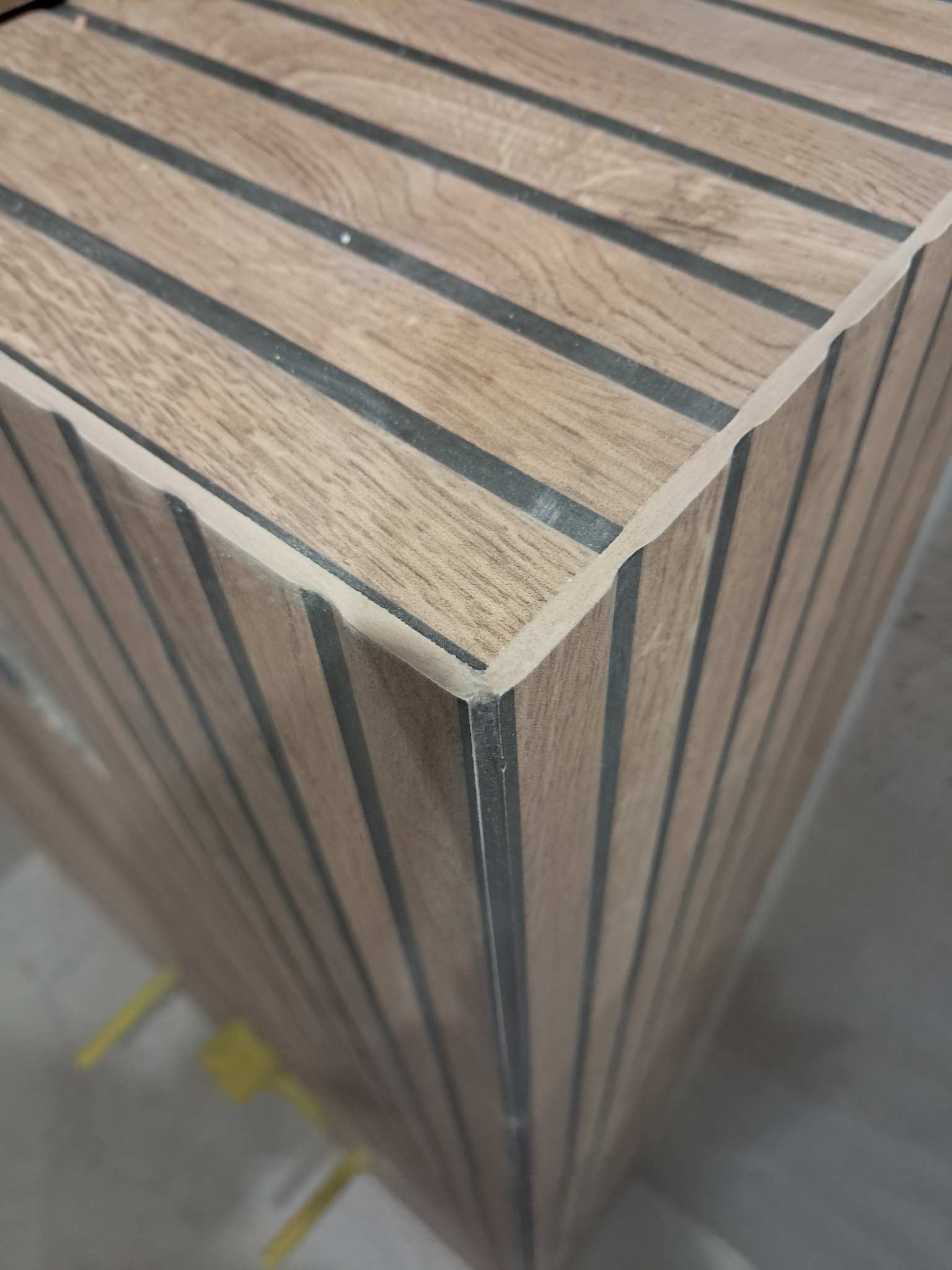 Wykończony narożnik obudowy z paneli drewnopodobnych z czarnymi fugami, widoczny z bliska pod kątem, ukazujący precyzję wykonania i estetykę detalu.