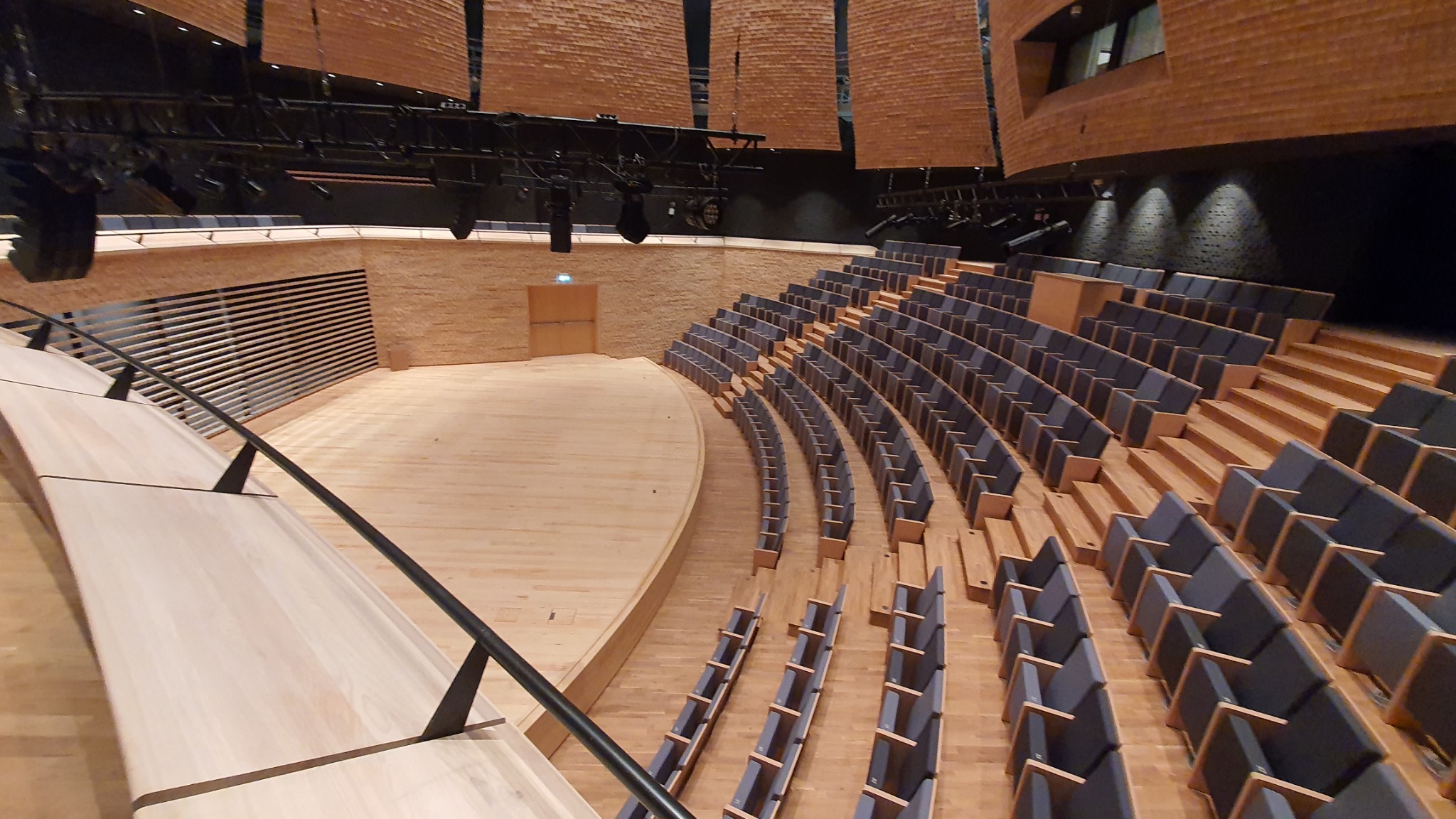 Sala koncertowa w Otwocku z drewnianą sceną, rzędami krzeseł i oświetleniem. Ujęcie z góry podkreśla przestronność i symetrię wnętrza.