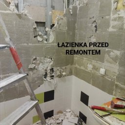 Daniel Strączek - Łazienka w trakcie demontażu płytek, widoczne fragmenty ścian z resztkami kleju, drabina i gruz. Przygotowanie do remontu z widocznymi elementami konstrukcyjnymi.