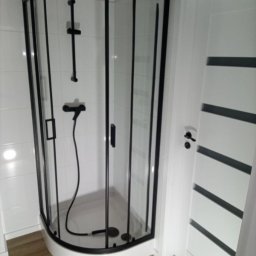 Daniel Strączek - Nowoczesna kabina prysznicowa z czarnymi ramami i białą armaturą, po remoncie. Widoczna biała ściana z płytkami i drzwi z poziomymi, czarnymi paskami.