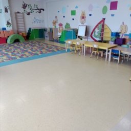 Daniel Strączek - Jasne wnętrze sali zabaw z kolorowymi malunkami na ścianach, niskimi stolikami i krzesłami. Podłoga w odcieniach beżu. Widoczne elementy wyposażenia i dekoracji.