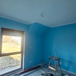 Daniel Strączek - Pomieszczenie po malowaniu ścian na błękitno, widoczne narzędzia malarskie i drabina. Ściany świeżo pomalowane, okno z roletami wpuszcza światło.