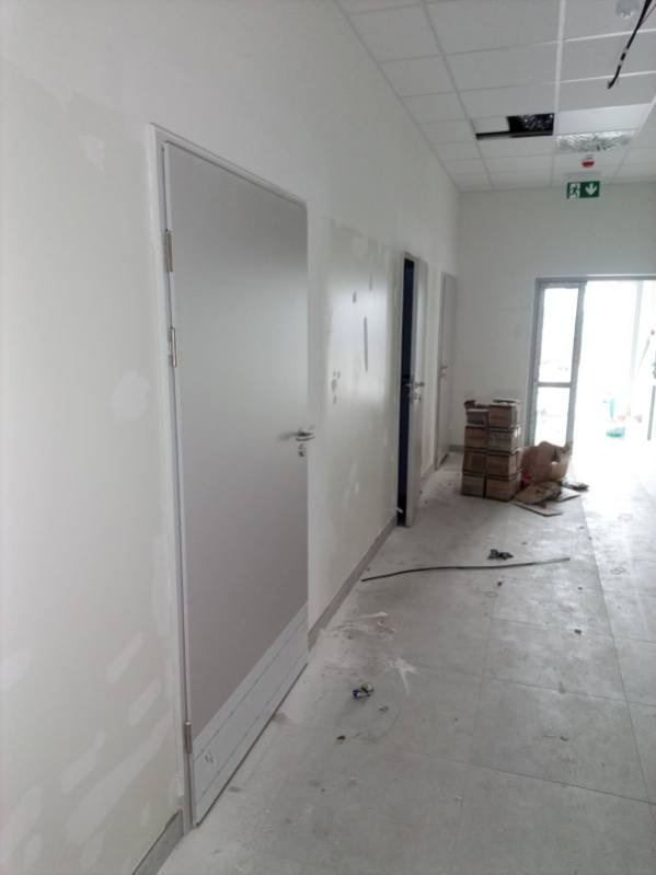 Korytarz w trakcie wykańczania: świeżo pomalowane ściany z widocznymi śladami szpachlowania, zamontowane drzwi i sufit podwieszany. Na podłodze widoczne ślady po remoncie.