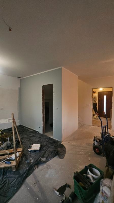 Wnętrze w trakcie prac: ściana pomalowana na szaro, widoczne narzędzia, folia ochronna na podłodze, przygotowania do dalszych prac wykończeniowych.