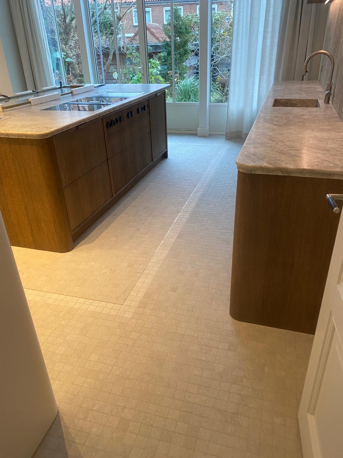 Jasna mozaika podłogowa w kuchni z drewnianą wyspą i blatem z marmuru. Widok na ogród przez duże okna. Nowoczesny design.