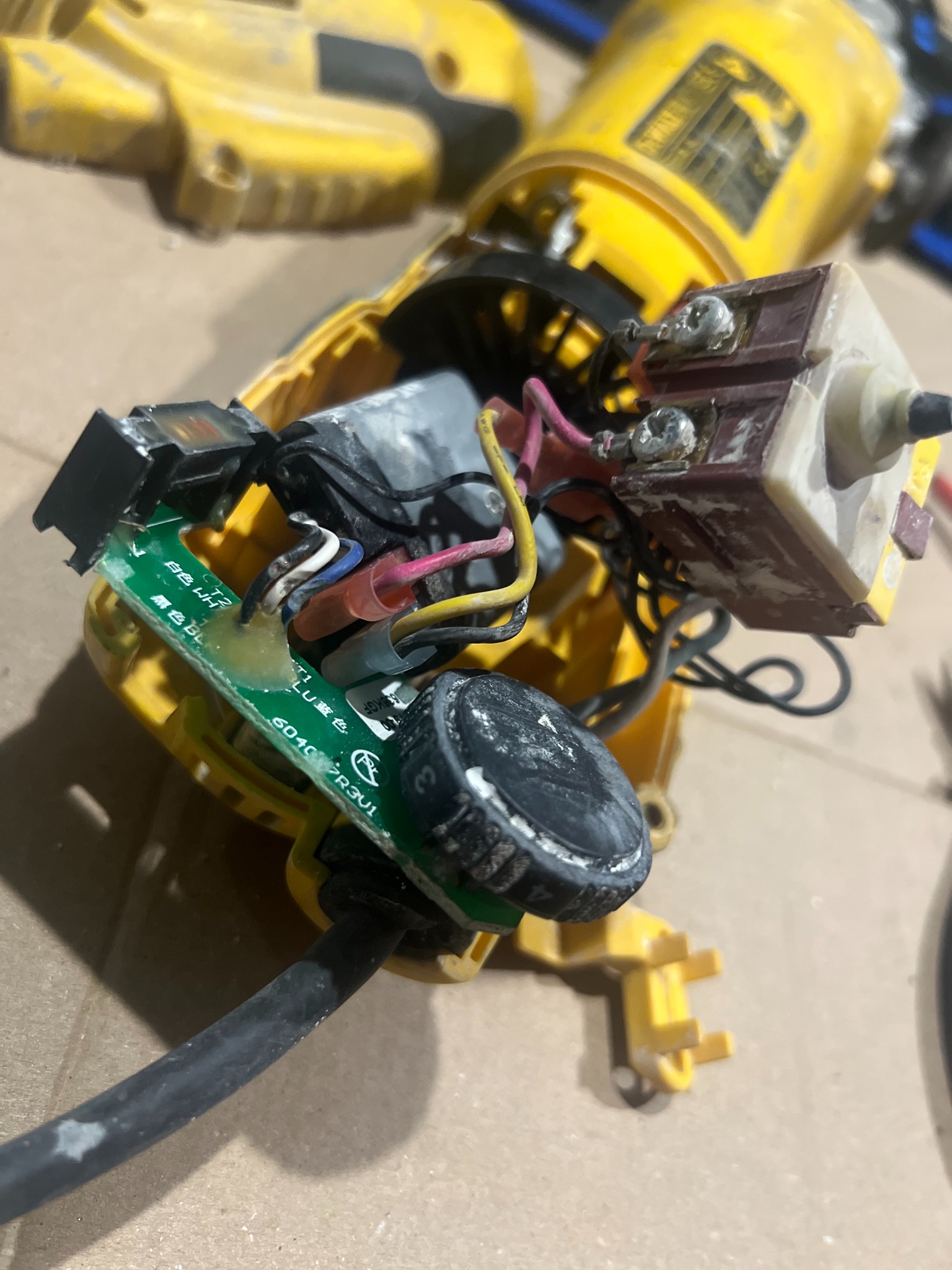 Otwarta obudowa żółtej szlifierki kątowej DeWalt z widocznymi elementami elektroniki, przewodami i przełącznikiem. Detal naprawy lub diagnostyki elektronarzędzia.