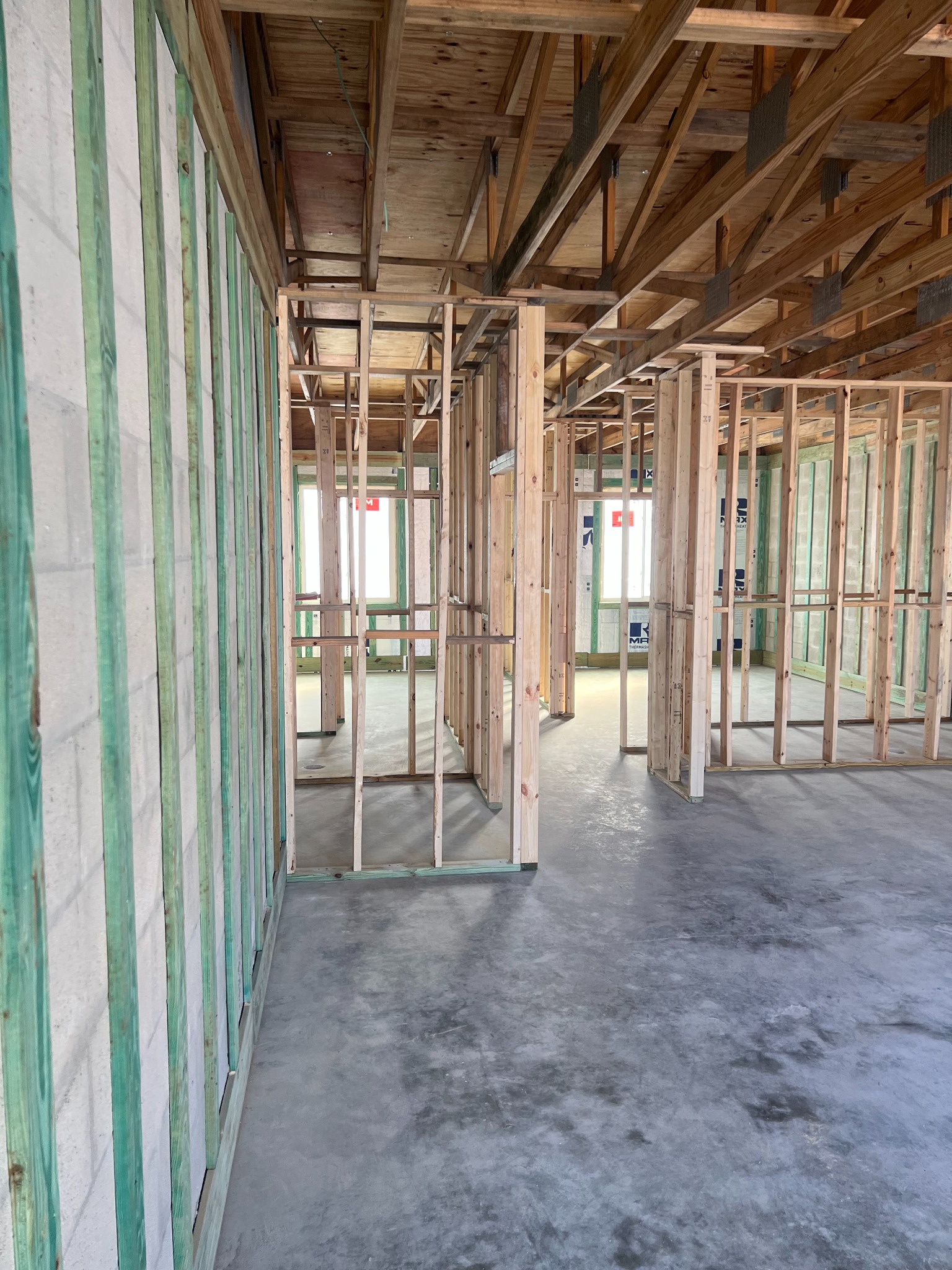 Surowy stan budynku szkieletowego: drewniana konstrukcja ścian, stropu i podłogi na betonowej wylewce, widoczne okna. Ściany z zielonymi elementami wzmacniającymi.
