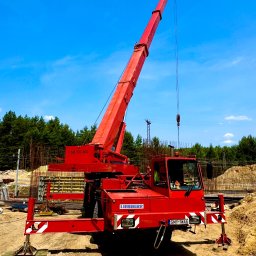 MONIX - Czerwony dźwig Liebherr na placu budowy z widocznymi elementami konstrukcyjnymi i błękitnym niebem w tle, z wysuniętymi podporami stabilizującymi.