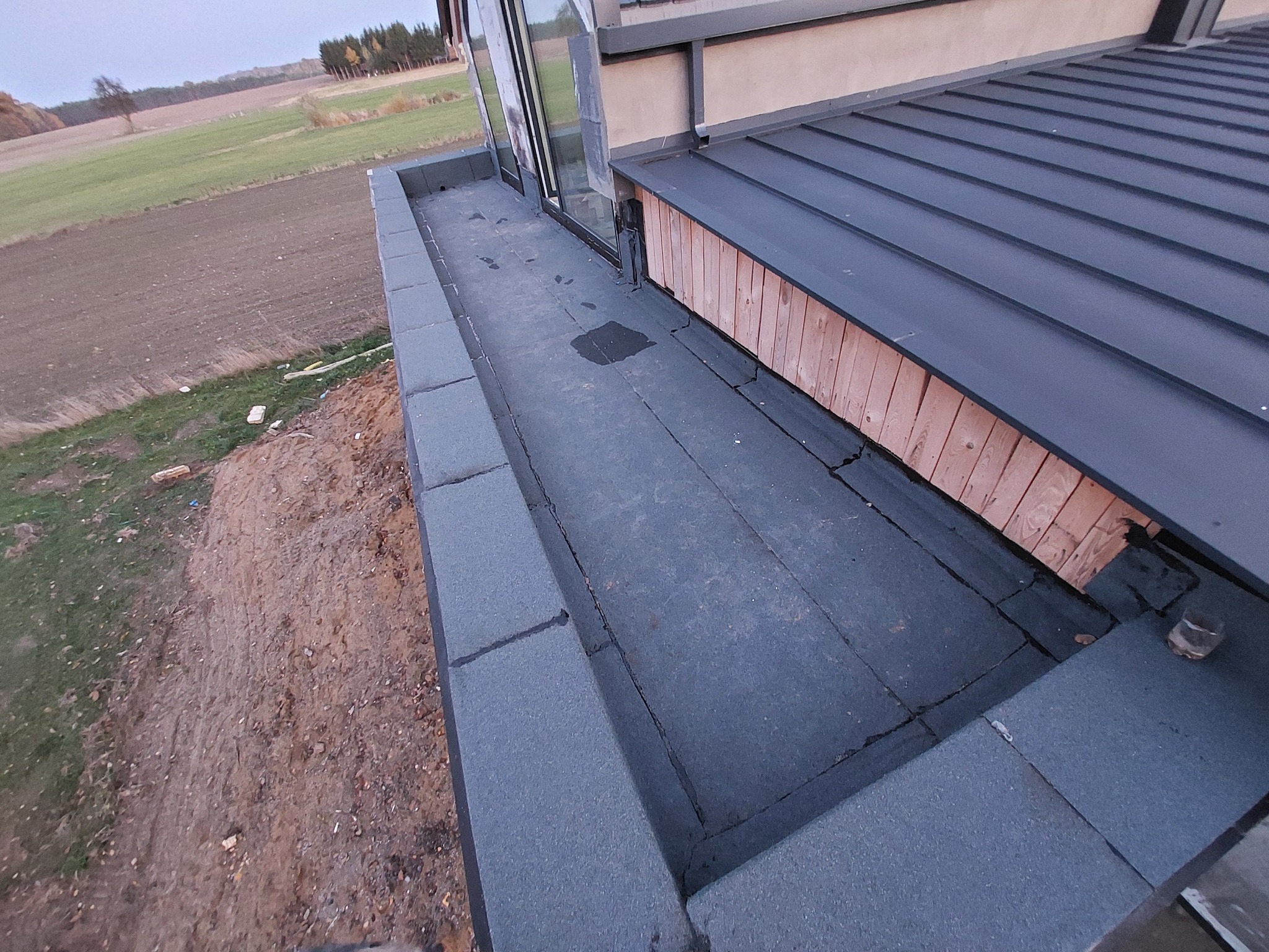 Wykończony dach z blachy na rąbek stojący, z detalami obróbek blacharskich przy oknie i drewnianą obudową. Widok z góry na gotową konstrukcję.