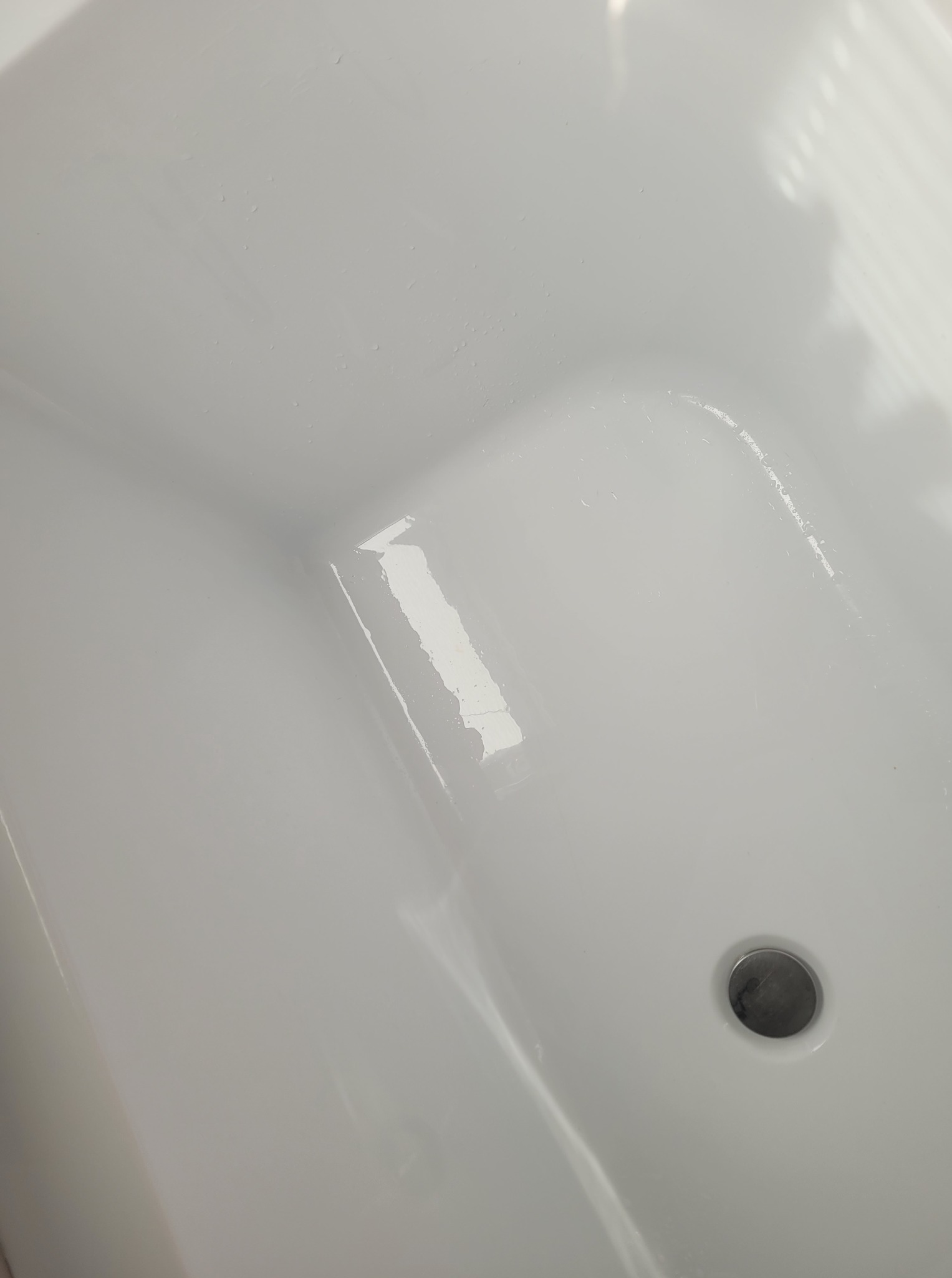 Biała umywalka z odpływem, widoczna z góry, oświetlona naturalnym światłem. Czysta powierzchnia z delikatnymi refleksami. Minimalistyczny design.