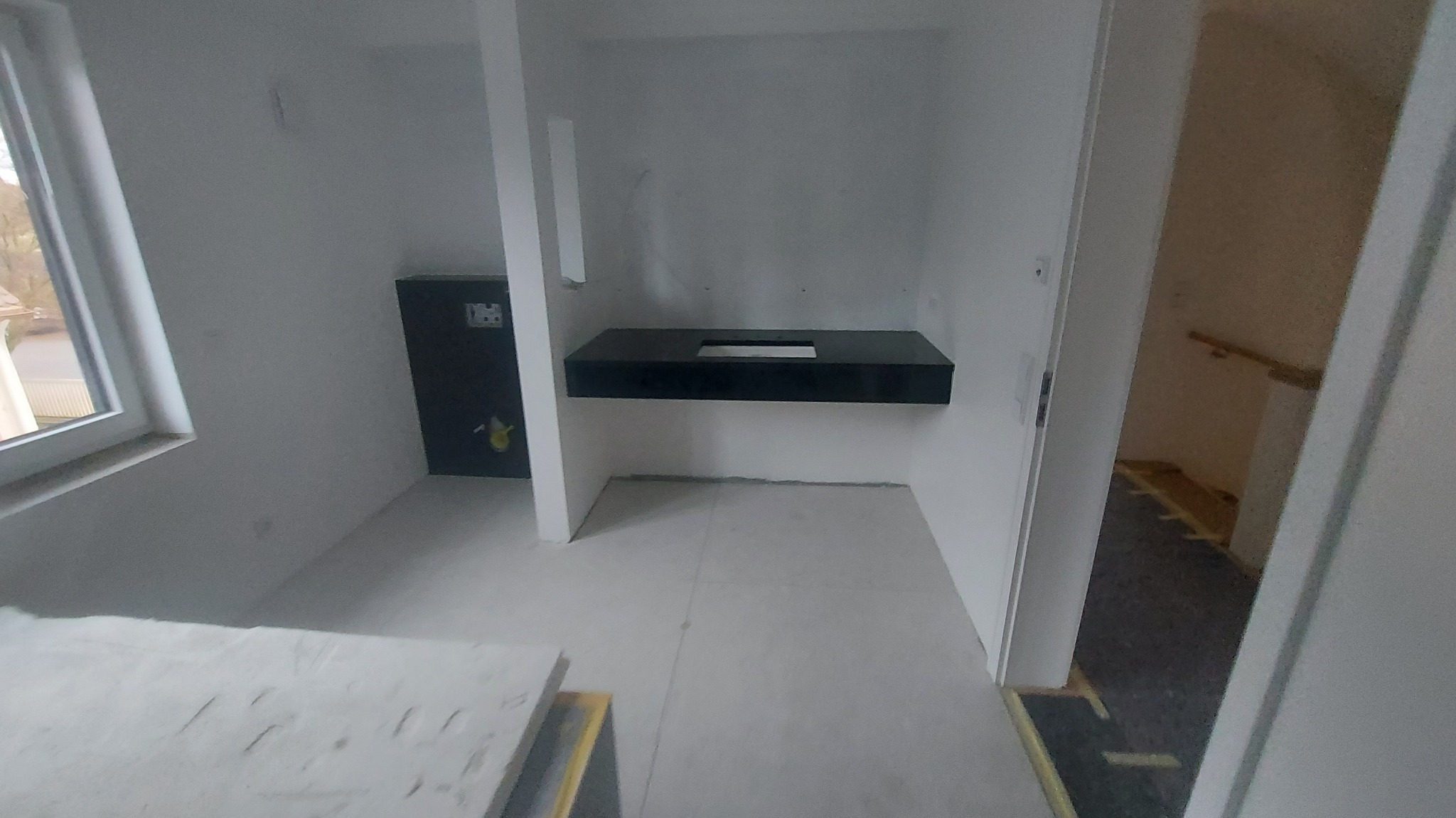 Surowy stan łazienki w Szepietowie: czarny blat umywalki zamontowany na ścianie, widoczna instalacja podtynkowa, przygotowana do dalszych prac wykończeniowych.