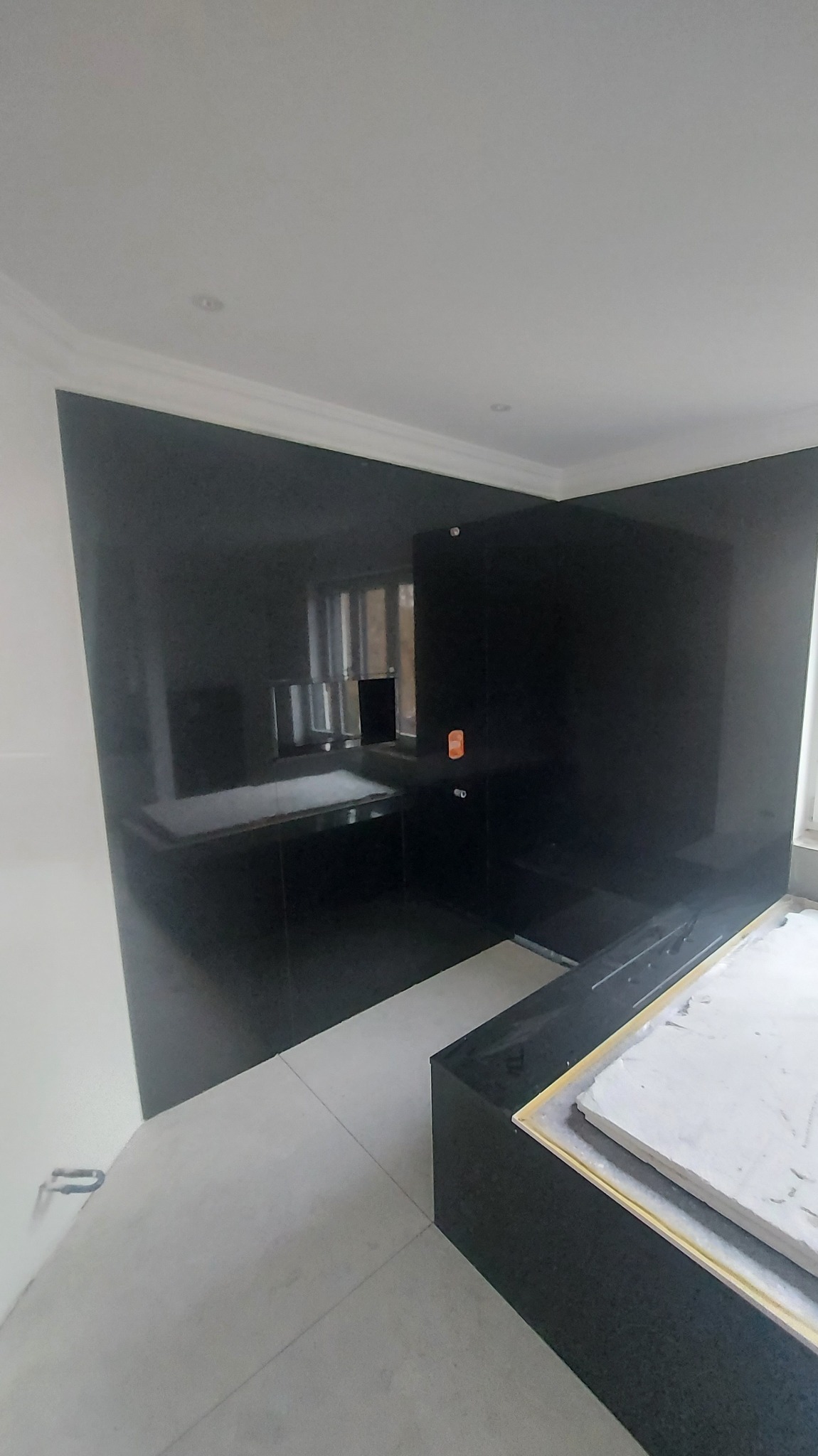 Nowoczesna łazienka z czarnymi, błyszczącymi płytami na ścianach, jasną podłogą i białym sufitem z dekoracyjną listwą. Minimalistyczny design.