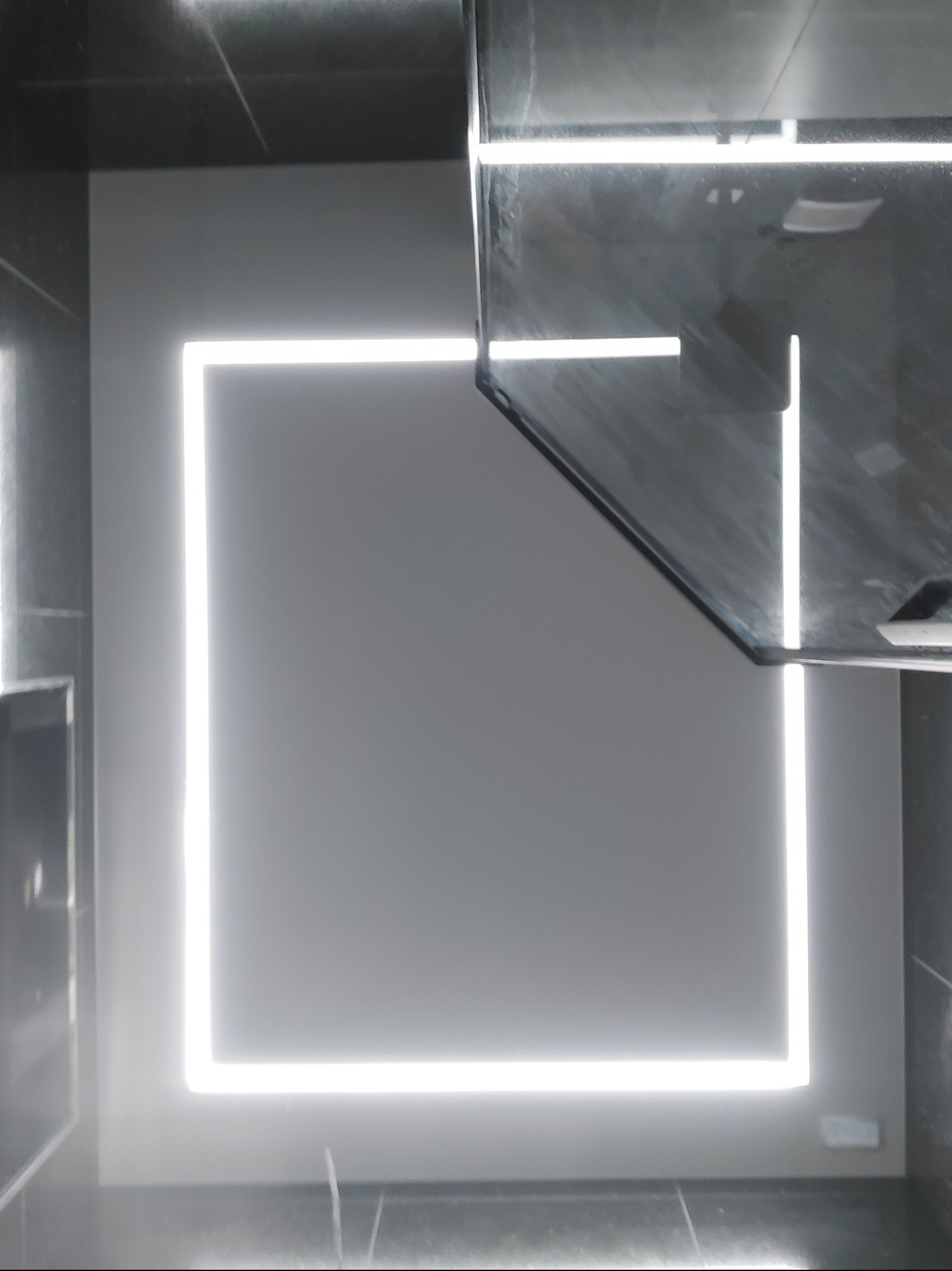 Nowoczesna łazienka z podświetlanym lustrem w kształcie kwadratu, czarne płytki na ścianach i podłodze, minimalistyczny design, oświetlenie LED.