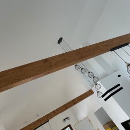Michał Kozłowski - Białe wnętrze ze skośnym sufitem, drewnianymi belkami i nowoczesnym oświetleniem. Widok z dołu ukazuje detale wykończenia i minimalistyczny design.