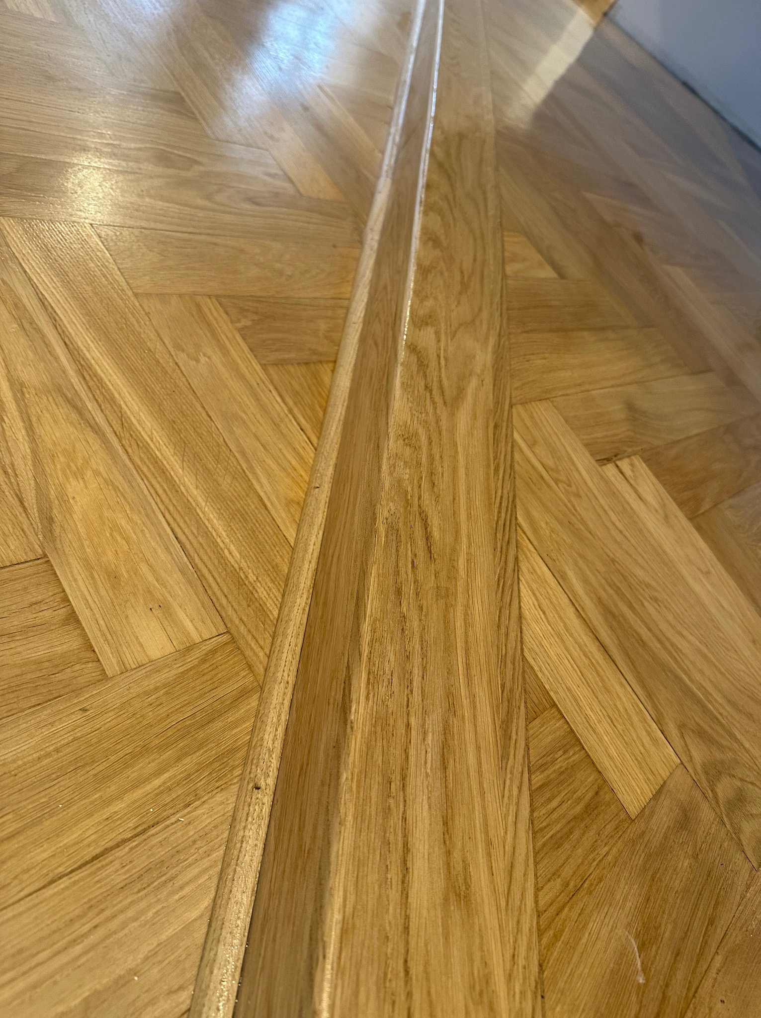 Parkiet ułożony w jodełkę, świeżo po cyklinowaniu, z widoczną listwą dylatacyjną. Efekt połysku podkreśla naturalny odcień drewna.