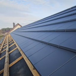 PROFESJONALNE DEKARSTWO - Nowy, grafitowy dach z blachy trapezowej w trakcie montażu, widok z dołu na drewnianą konstrukcję i częściowo pokrytą powierzchnię. Ujęcie pod kątem.