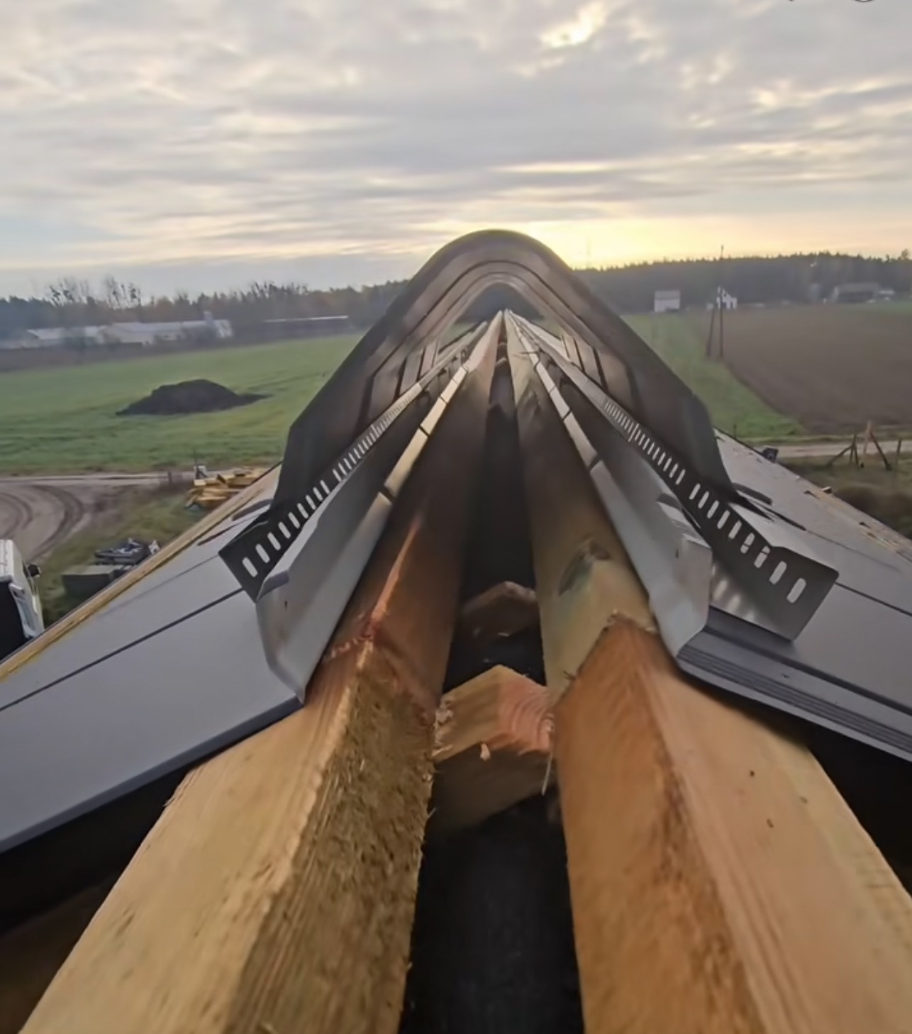 Wiązar dachowy z metalowymi elementami w trakcie montażu, widok z góry na konstrukcję dachu na tle krajobrazu. Elementy montażowe z bliska.