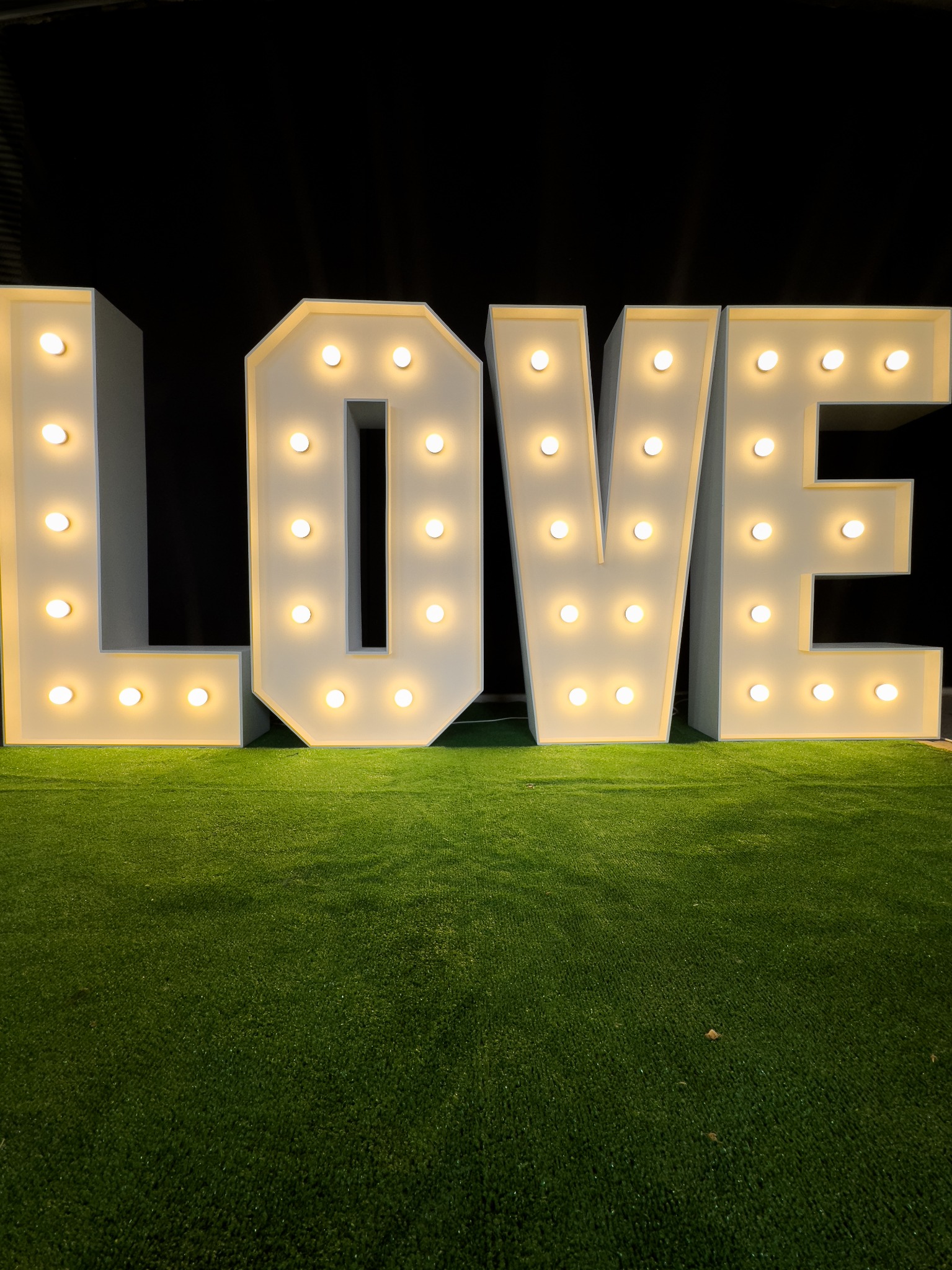 Dekoracyjne, podświetlane litery LOVE na sztucznej trawie, tworzące romantyczną atmosferę. Idealne na wesele lub sesję zdjęciową.