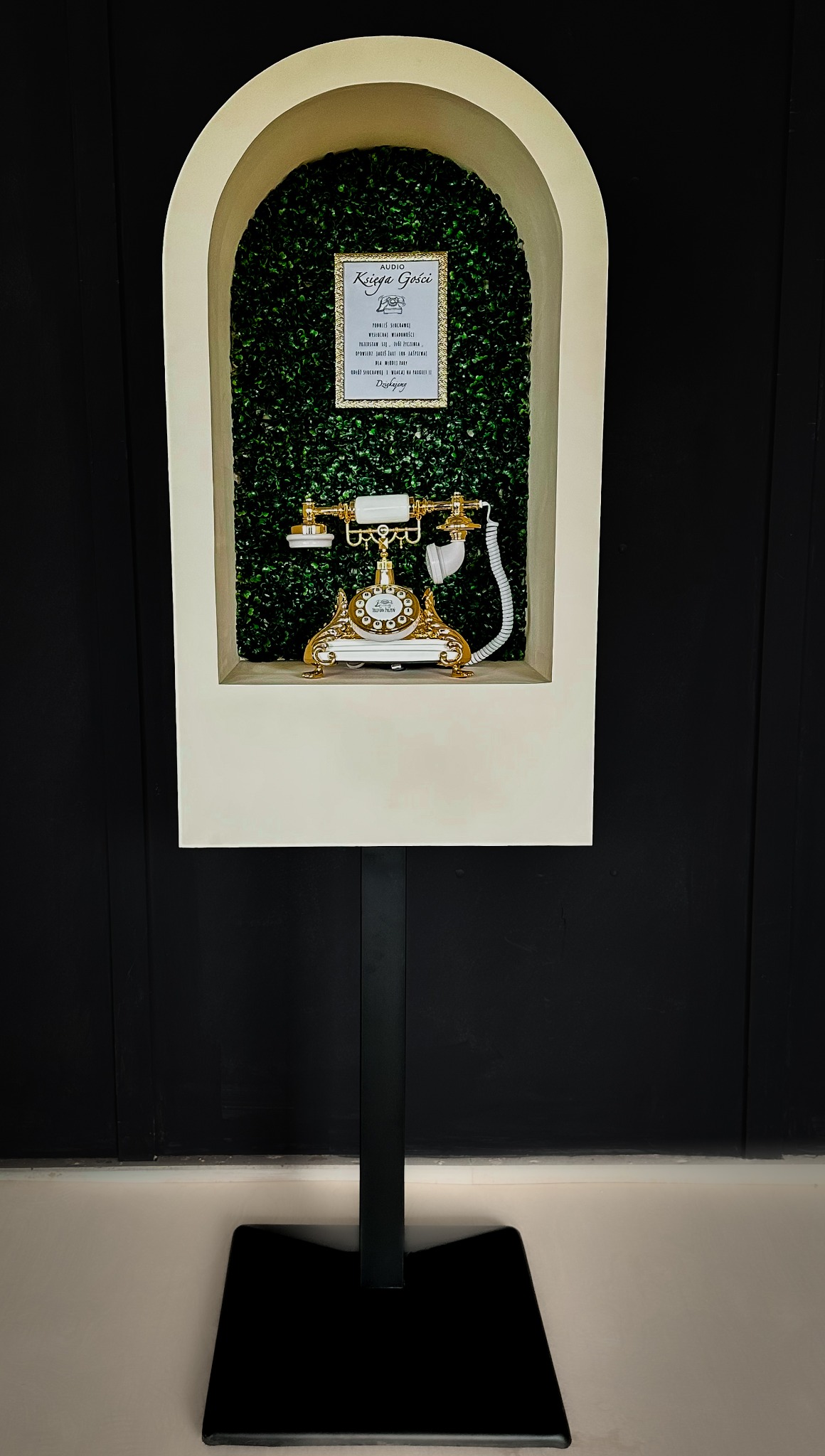 Instalacja artystyczna: złoty telefon retro w niszy z zielenią i napisem 'Audio Księga Gości', całość na czarnym tle, element dekoracyjny eventu.