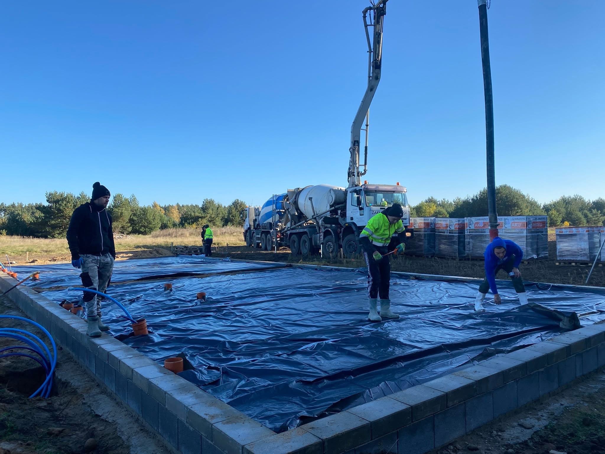 Fundamenty pod dom jednorodzinny z izolacją poziomą i pionową, przygotowane do wylania betonu. Prace budowlane we Władysławowie. Widoczny betonowóz.