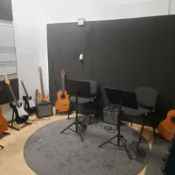 Studio muzyczne w Słupsku z gitarami akustycznymi i elektrycznymi, wzmacniaczami, pulpitami na nuty. Wykładzina tłumiąca dźwięk na ścianach.