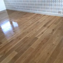 Jasny, błyszczący parkiet ułożony w eleganckim wzorze, odbijający światło okna. Ściana w romby w odcieniach szarości i błękitu. Nowoczesne wykończenie podłogi.