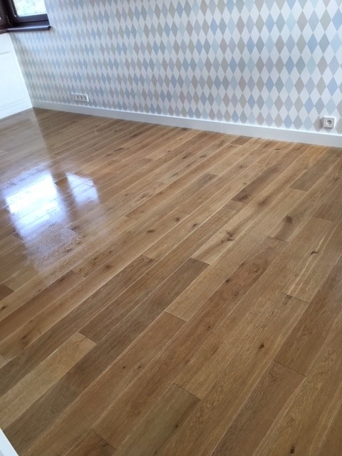 Jasny, błyszczący parkiet ułożony w eleganckim wzorze, odbijający światło okna. Ściana w romby w odcieniach szarości i błękitu. Nowoczesne wykończenie podłogi.