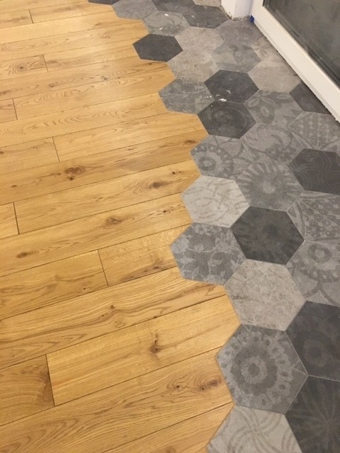 Parkiet z jasnego drewna zestawiony z szarymi heksagonalnymi płytkami, tworząc nowoczesną i stylową podłogę w pomieszczeniu.