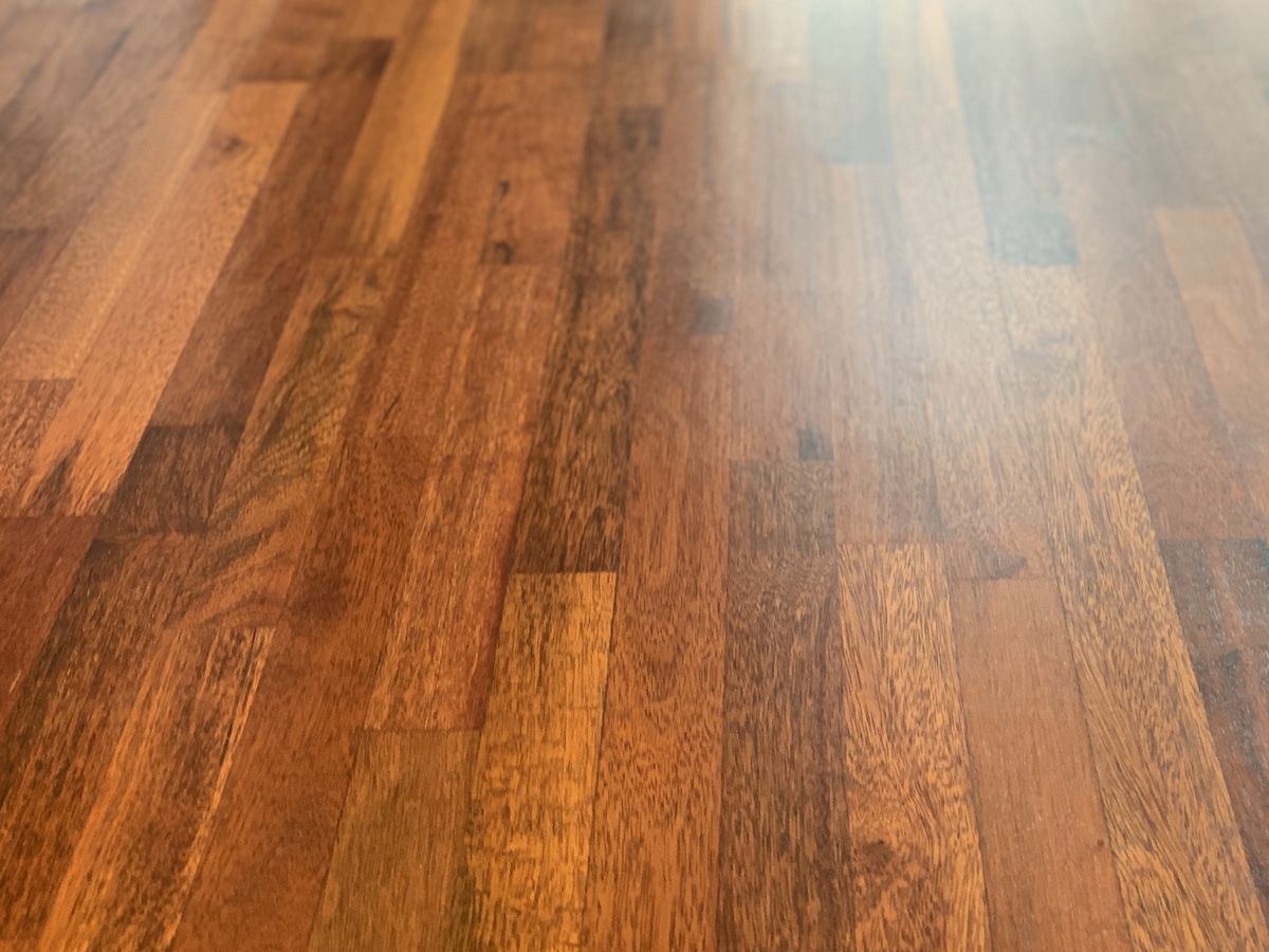 Połyskująca, świeżo polakierowana podłoga z ciemnego drewna, parkiet ułożony w regularny wzór, widok pod kątem, delikatne odbicie światła.