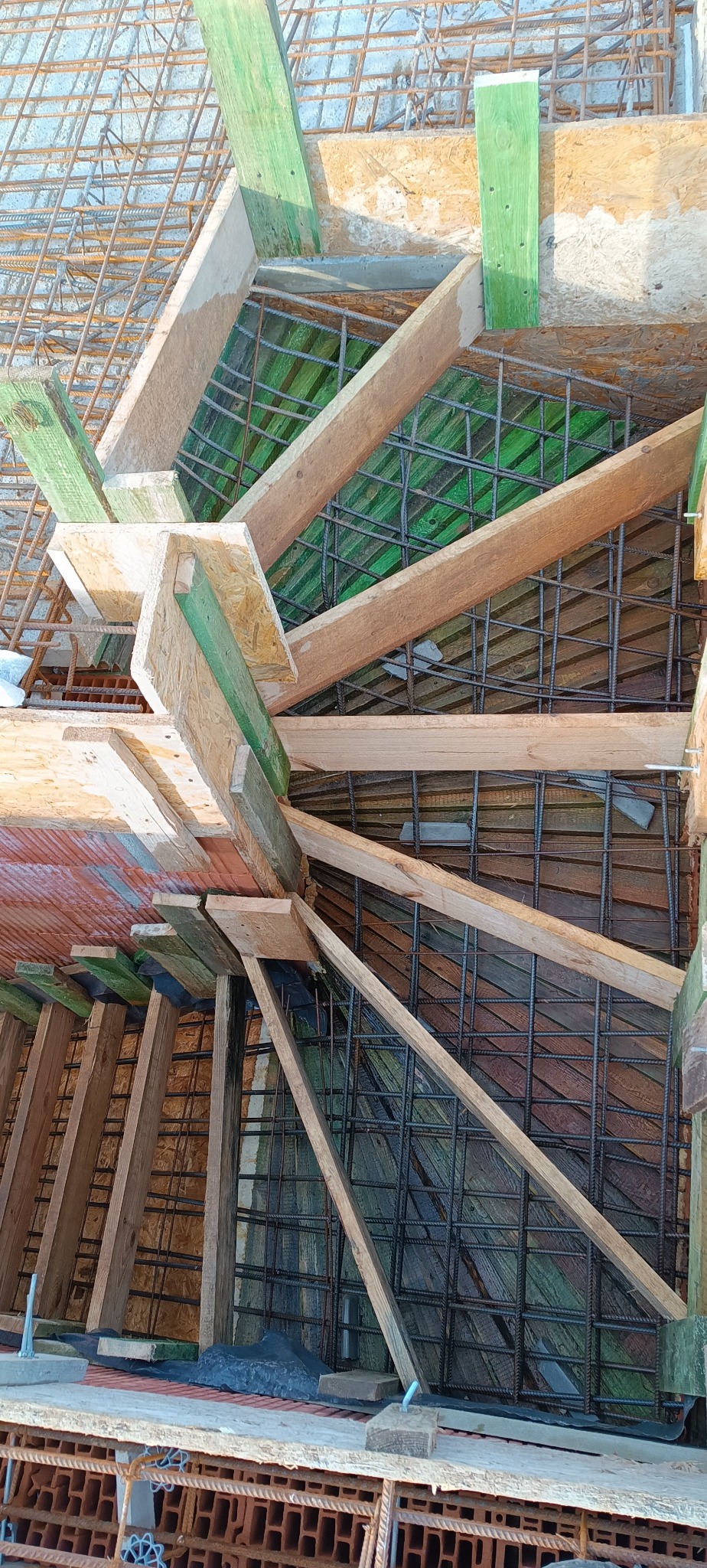 Skomplikowane zbrojenie schodów z drewnianym szalunkiem, widok z góry na budowie. Metalowe pręty tworzą siatkę, drewniane elementy konstrukcyjne.