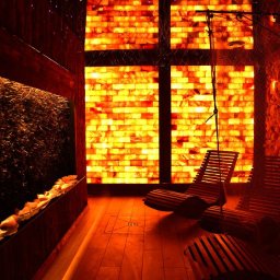 SOMA SPÓŁKA Z OGRANICZONĄ ODPOWIEDZIALNOŚCIĄ - Komnata solna z tężnią solankową, oświetlona panelami z soli himalajskiej. W tle drewniane leżaki relaksacyjne i ściana z brył soli.