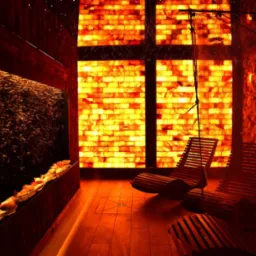 Komnata solna z tężnią solankową, oświetlona panelami z soli himalajskiej. W tle drewniane leżaki relaksacyjne i ściana z brył soli.