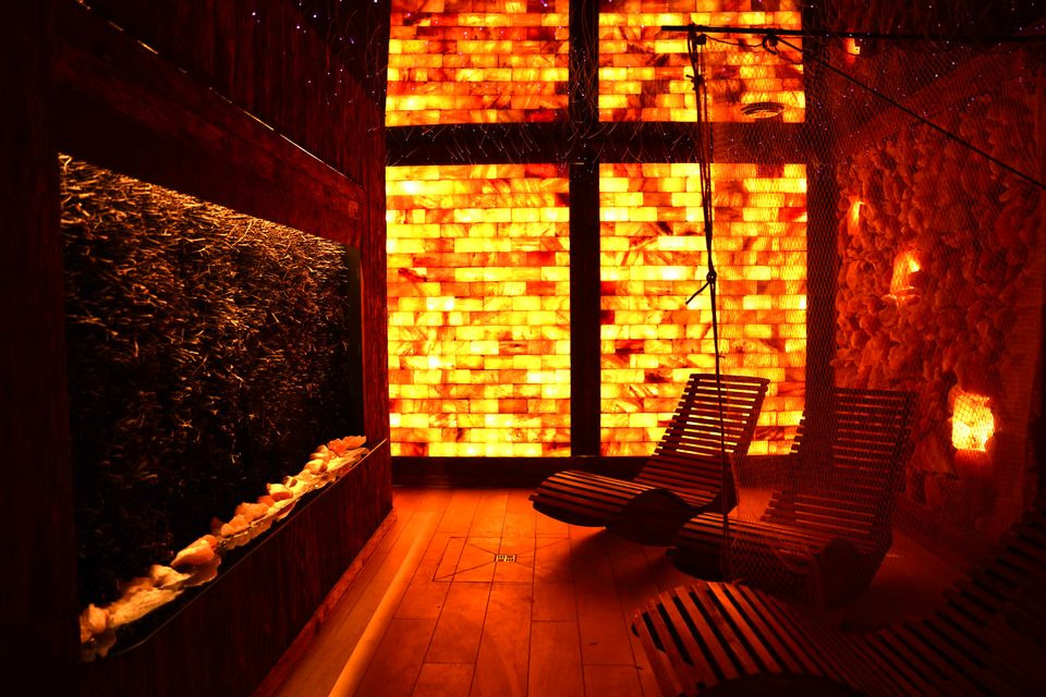 Komnata solna z tężnią solankową, oświetlona panelami z soli himalajskiej. W tle drewniane leżaki relaksacyjne i ściana z brył soli.
