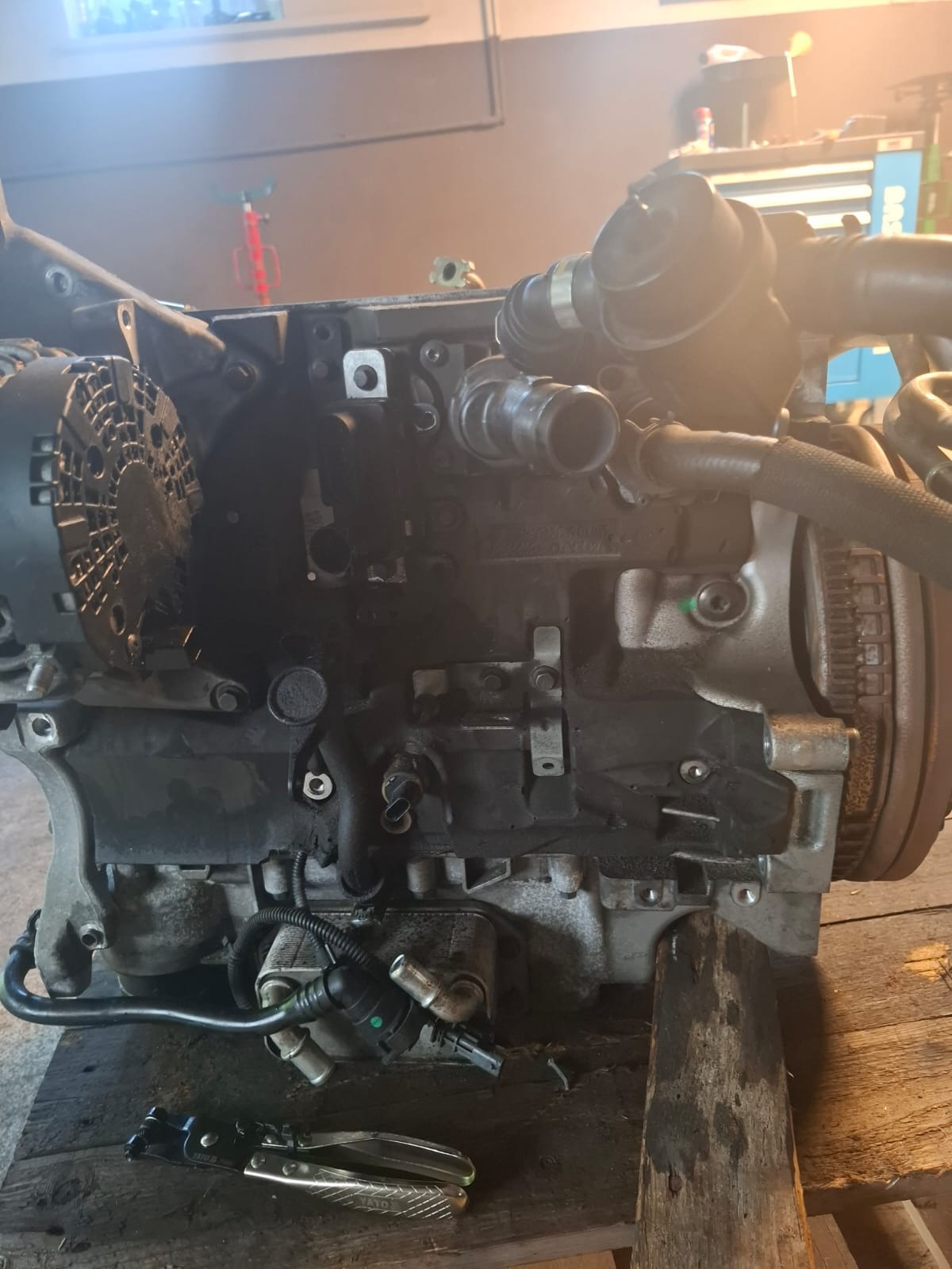 Silnik samochodowy na drewnianym blacie, widoczne przewody, alternator i narzędzia. Ujęcie z bliska, oświetlenie warsztatowe.