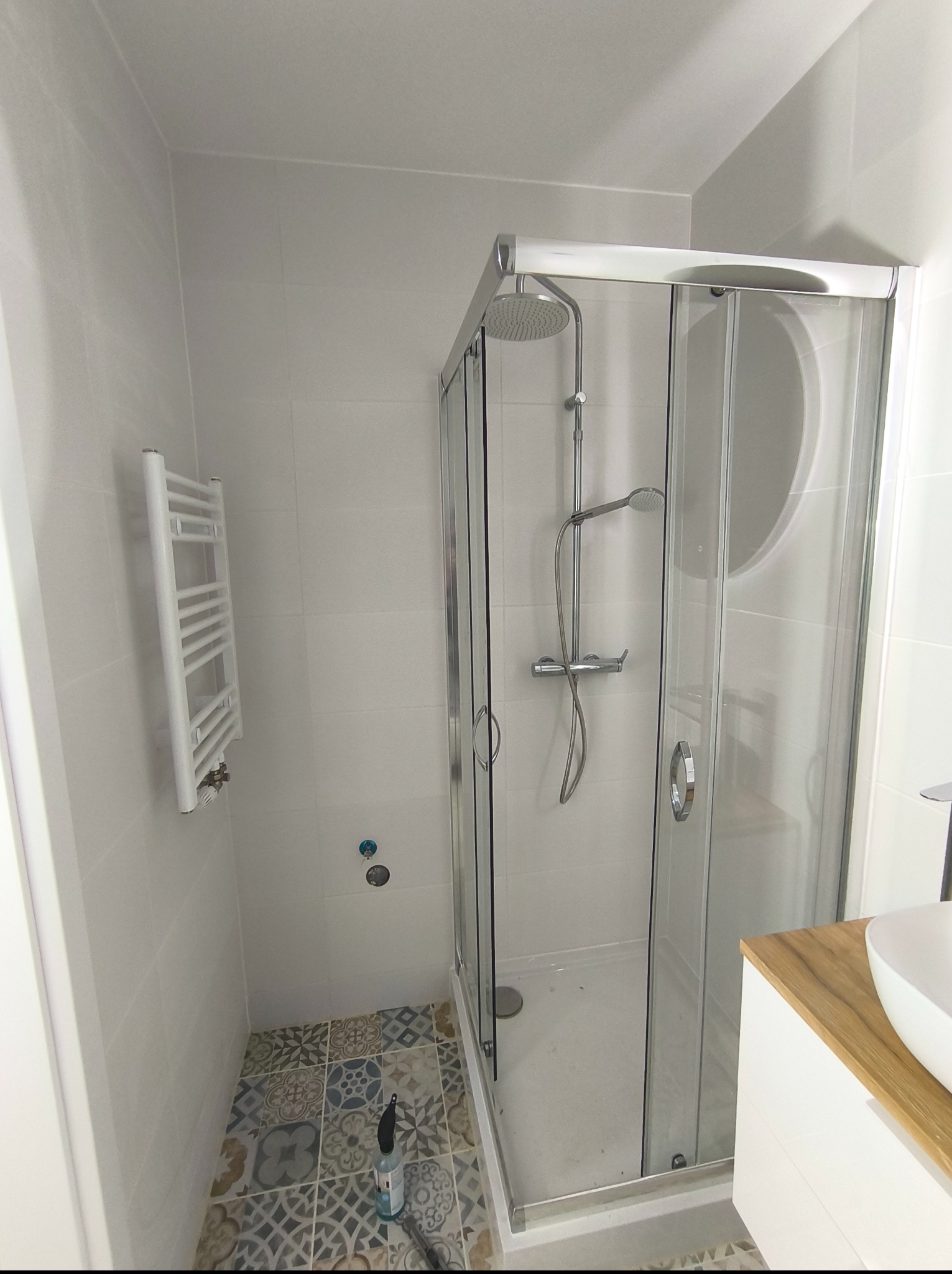 Nowoczesna kabina prysznicowa z chromowanymi detalami i deszczownicą, białe płytki ścienne i dekoracyjne płytki podłogowe w łazience po remoncie.