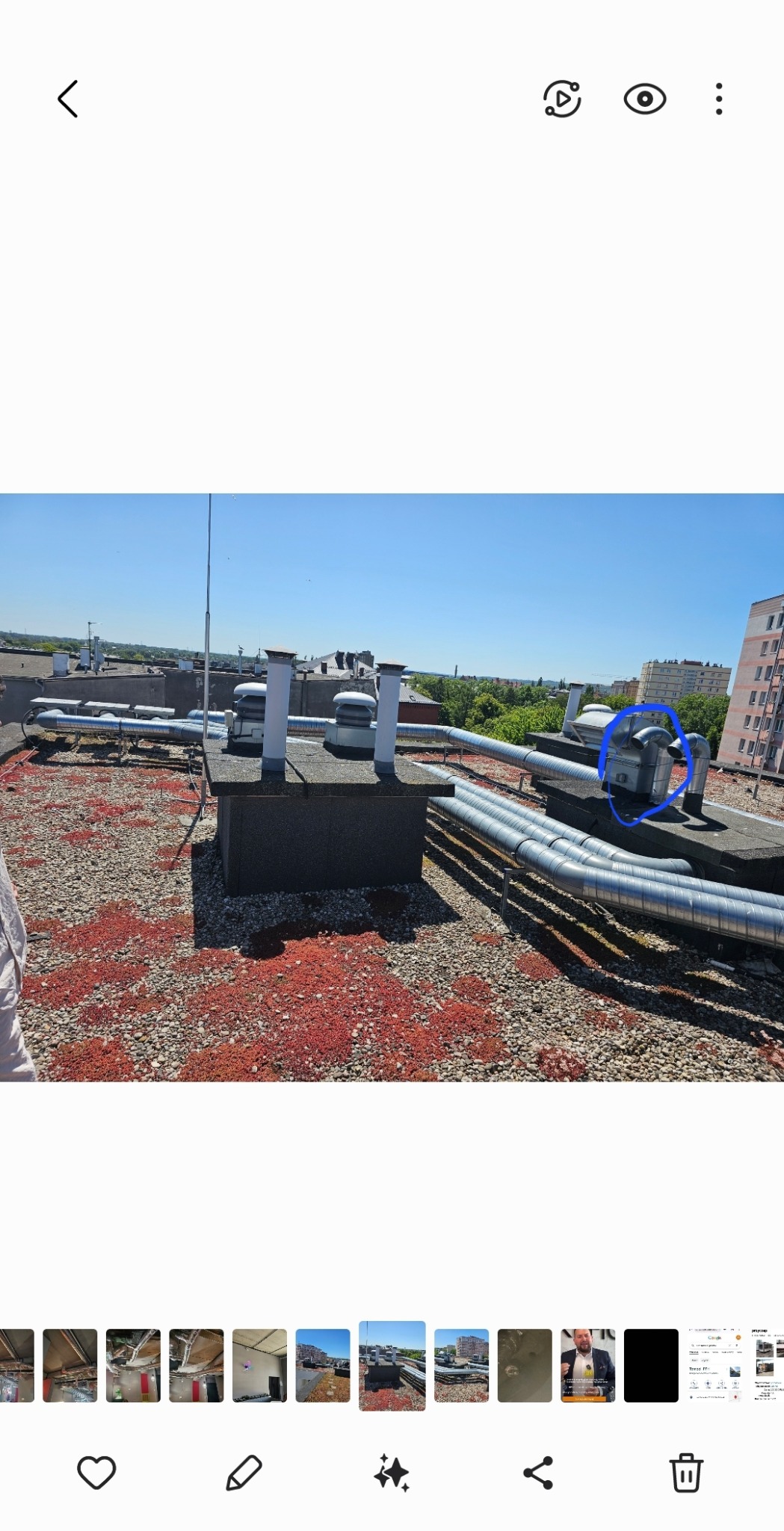 Instalacja wentylacyjna na dachu budynku z widocznymi rurami i elementami systemu. Dach pokryty czerwoną nawierzchnią. Jasne, słoneczne światło dnia.