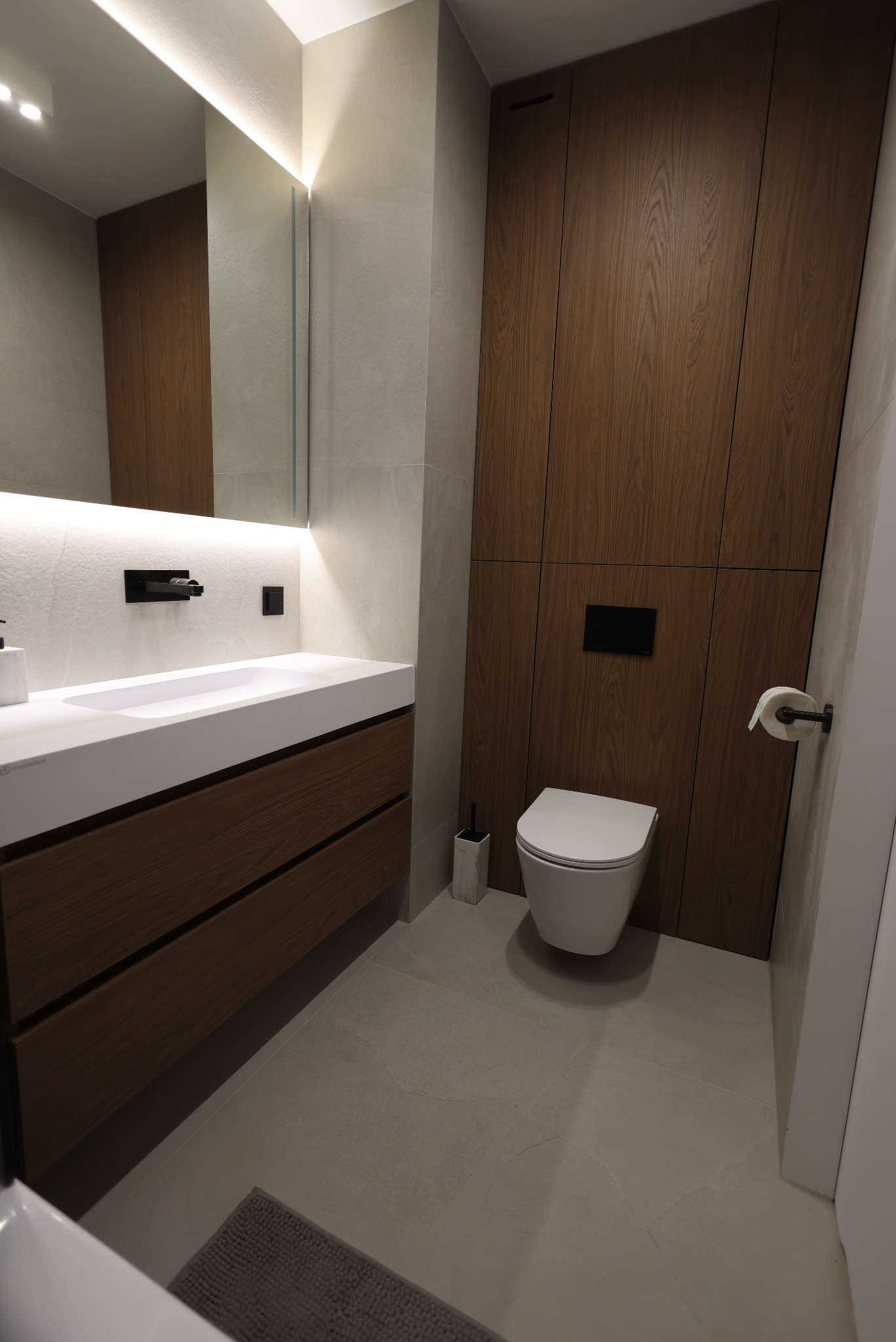 Nowoczesna łazienka z drewnianą zabudową szafek i ukrytą spłuczką. Minimalistyczny design z podświetlanym lustrem i kamienną umywalką.