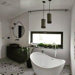 LOLEK Przedsiębiorstwo Handlowo Usługowe Marcin Plewak - Nowoczesna łazienka z wolnostojącą wanną, umywalką nablatową i lustrem o nieregularnym kształcie. Na podłodze lastryko, a nad wanną wiszą lampy cylindryczne.