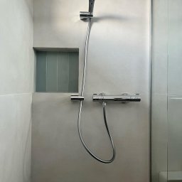 LOLEK Przedsiębiorstwo Handlowo Usługowe Marcin Plewak - Nowoczesna kabina prysznicowa z deszczownicą i wnęką z szarymi płytkami. Minimalistyczny design, jasne ściany, chromowana armatura. Widok na szklane drzwi kabiny.
