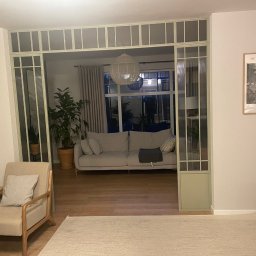 Sowiński - Wykończenia Wnętrz Mariusz Sowiński - Stylowe wykończenie wnętrza: salon z przeszklonymi drzwiami w odcieniach zieleni, beżowy dywan, sofa i fotel. Na ścianie plakat Henri Rousseau.