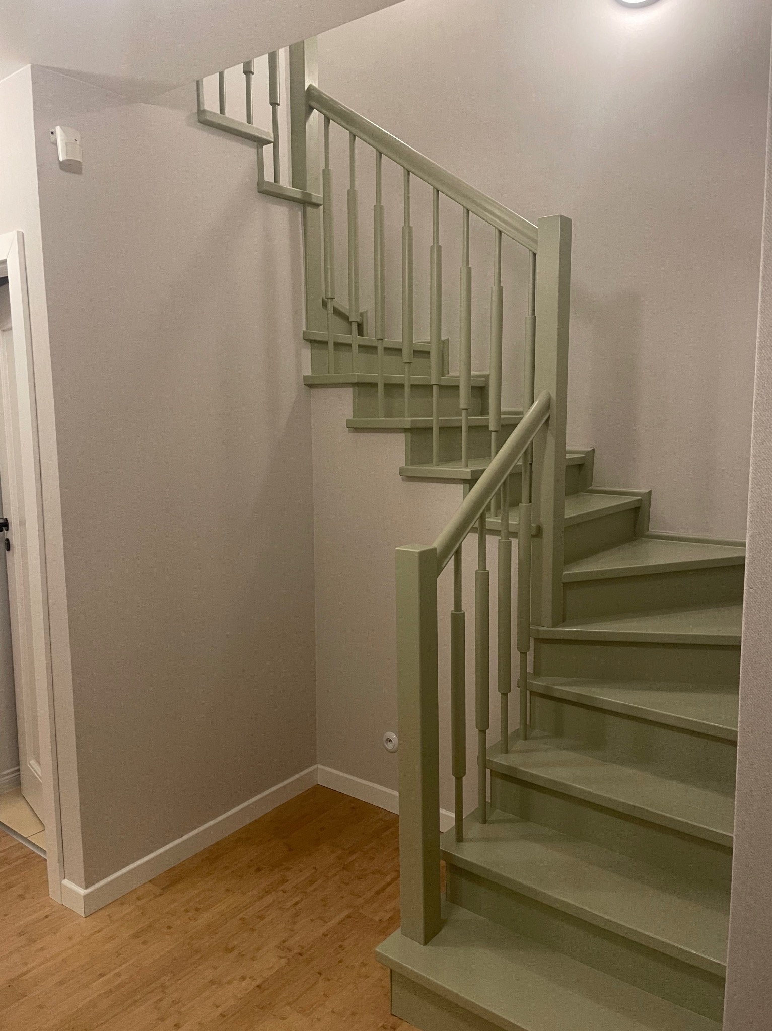 Klatka schodowa w odcieniach zieleni, drewniane schody spiralne z balustradą, jasne ściany i drewniana podłoga. Wykończenie wnętrza.