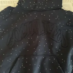 Czarna bluza z kapturem marki odzieżowej, zdobiona haftowanym napisem i licznymi, drobnymi dżetami. Widoczna kieszeń typu kangur i wykończenie dekoltu.